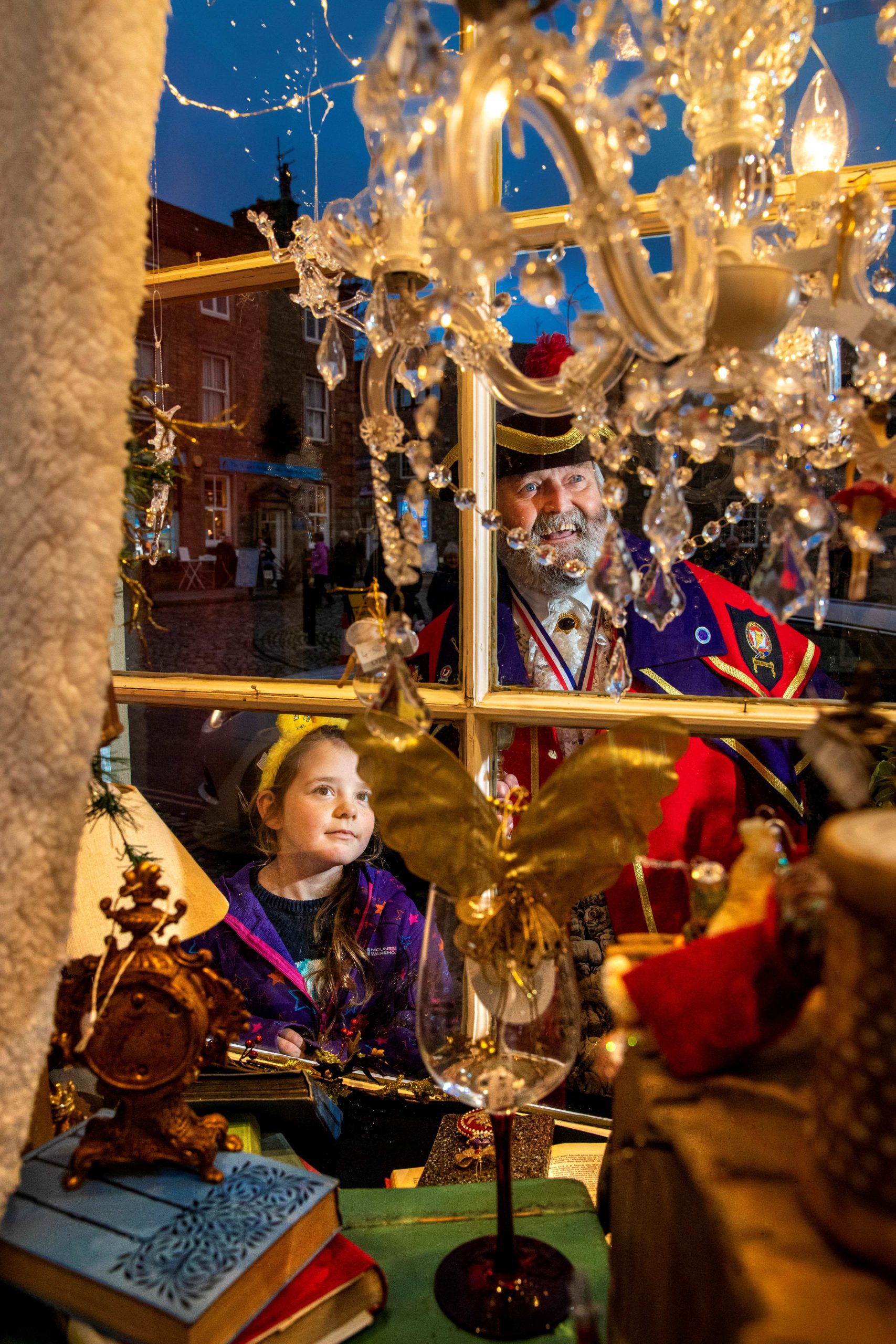Town cryer and little girl looking through a christmas window